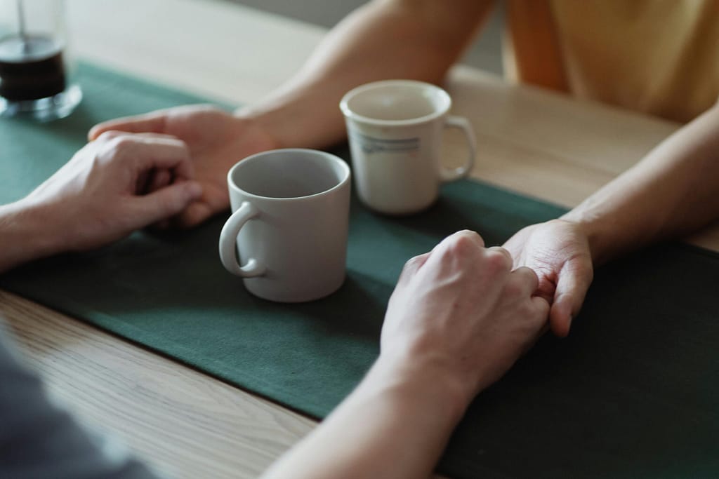 Close-up of hands holding across a table with coffee cups, conveying warmth and connection.