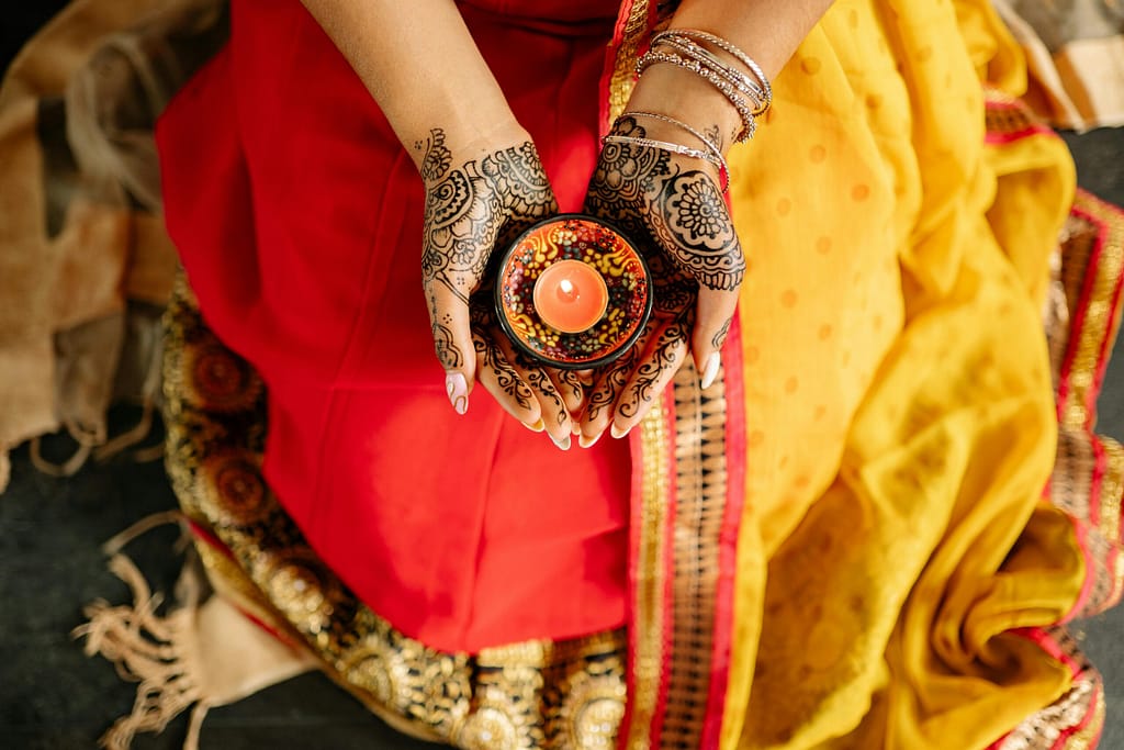 A woman in traditional attire holds a candle, symbolizing light and festivity during Diwali with intricate henna designs on her hands.