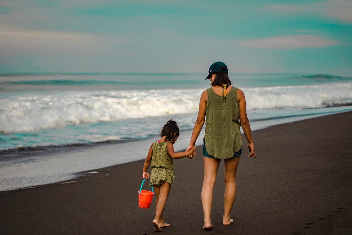 back view photo of woman and child holding hands while walking on beach