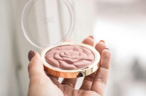 A delicate rose-shaped blush compact held in hand, perfect for enhancing your makeup collection.