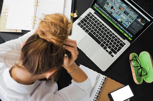 Overhead view of a stressed woman working at a desk with a laptop, phone, and notebooks.