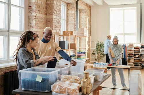 A diverse group of young adults volunteering at a donation center sorting clothes.