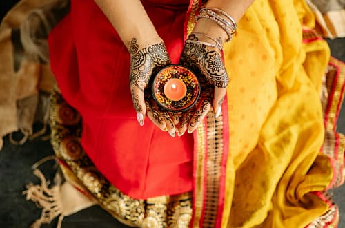 A woman in traditional attire holds a candle, symbolizing light and festivity during Diwali with intricate henna designs on her hands.
