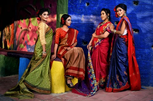 Group of women in vibrant Indian sarees posing against a colorful backdrop.