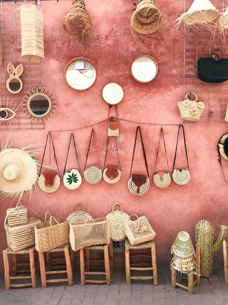 Aesthetic display of handmade wicker and straw accessories against a textured pink wall.